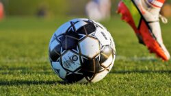 Dekat bola sepak dan kaki pemain selama pertandingan di lapangan berumput.