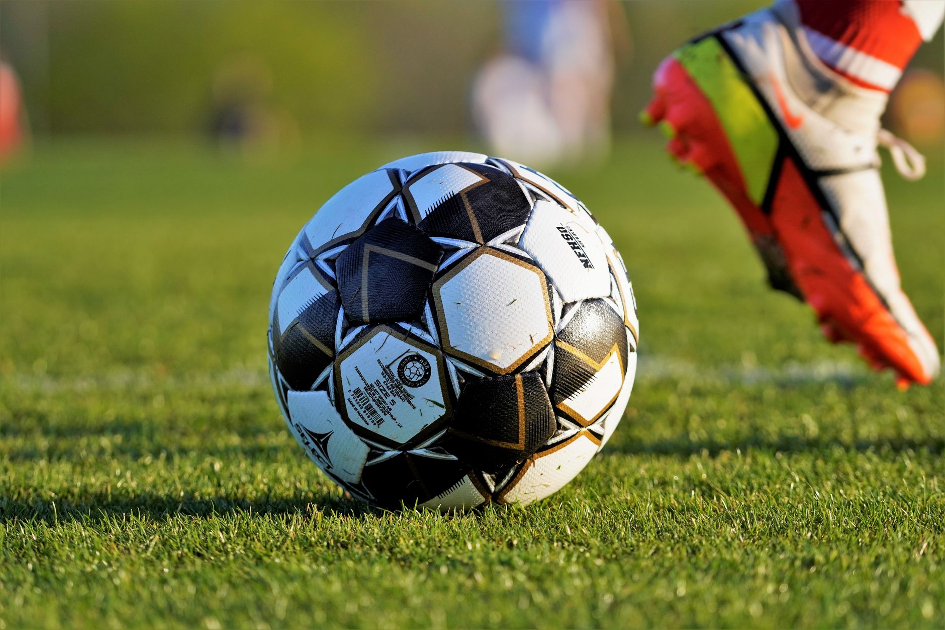 Dekat bola sepak dan kaki pemain selama pertandingan di lapangan berumput.