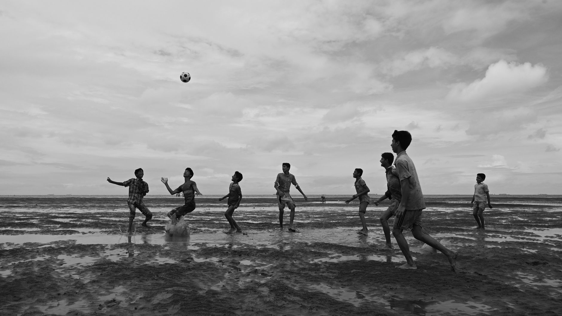 Sekelompok anak laki-laki yang bermain sepak bola dengan antusias di pantai di Chattogram, Bangladesh.