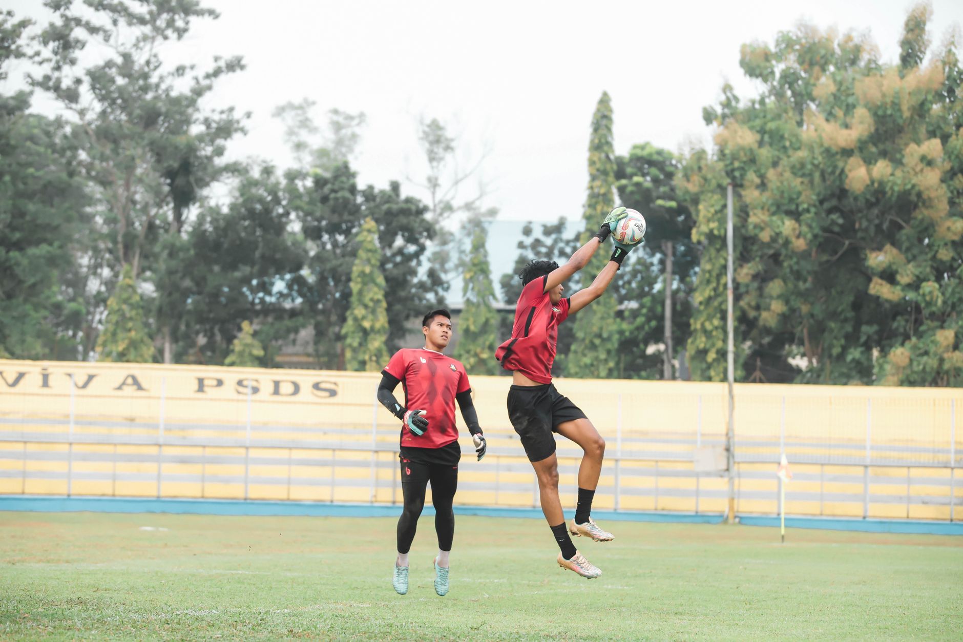 Atlet sedang bertindak selama sesi pelatihan sepak bola di luar ruangan, menampilkan lompatan energik dan kerja sama tim.