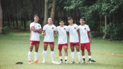 Sekel pemain sepak bola muda berpose dalam seragam tim di lapangan hijau yang subur. Pengaturan olahraga luar ruangan.