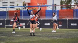 Para pemain wanita merayakan setelah mencetak gol dalam pertandingan flag football di lapangan terbuka yang semarak.