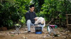 Seorang pria dewasa membuat batik menggunakan teknik tradisional di luar ruangan.