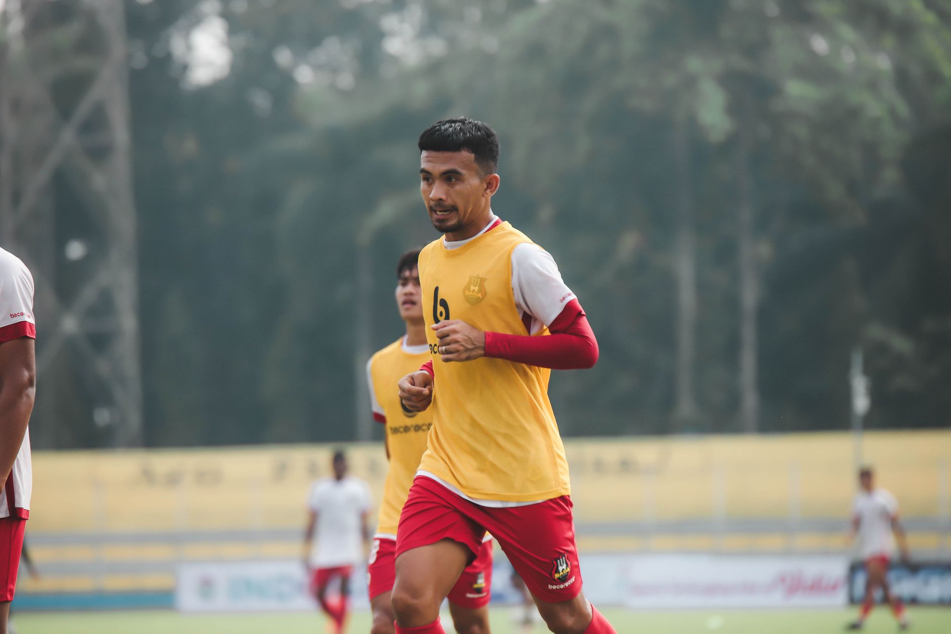 Pengambilan gambar dinamis seorang pemain sepak bola di tengah permainan di lapangan terbuka, menunjukkan tekad dan fokus.