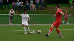 Pertandingan sepak bola penuh aksi dengan pemain yang bersaing di lapangan terbuka.