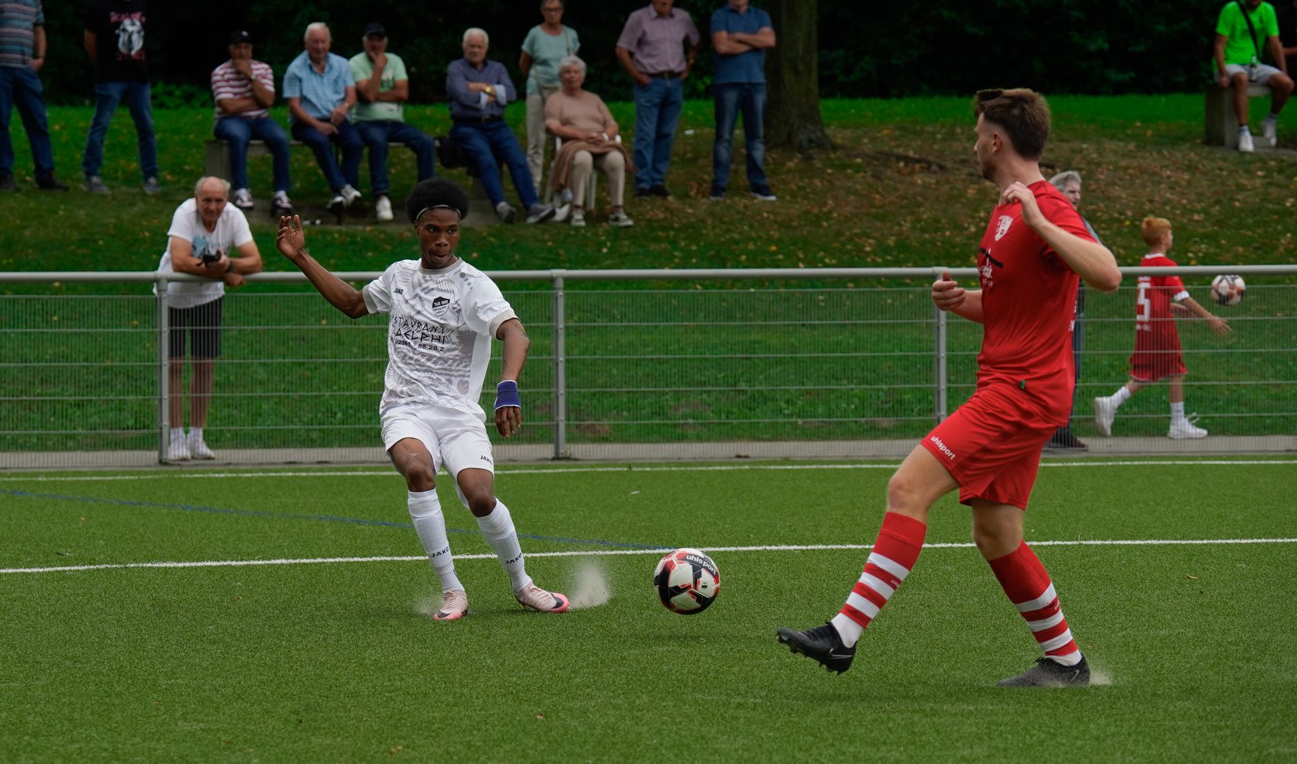 Pertandingan sepak bola penuh aksi dengan pemain yang bersaing di lapangan terbuka.