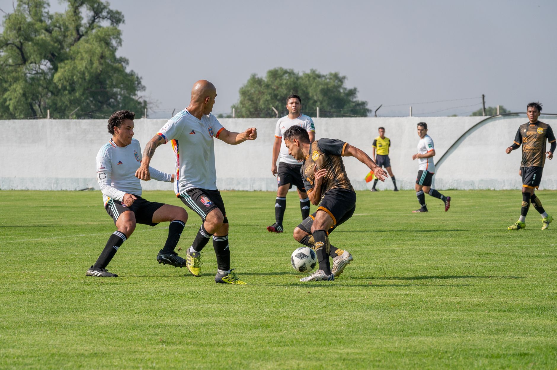 Pertandingan sepak bola dinamis dengan pemain bergerak di lapangan luar ruangan yang cerah.
