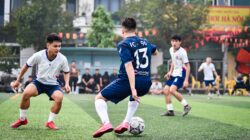 Pertandingan sepak bola dinamis di lapangan rumput buatan di Hanoi, yang menampilkan atletis dan semangat tim.