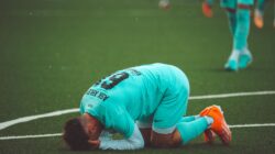 Seorang pemain sepak bola berlutut dalam keputusasaan di lapangan olah raga rumput sintetis hijau.