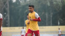 Pengambilan gambar dinamis seorang pemain sepak bola di tengah permainan di lapangan terbuka, menunjukkan tekad dan fokus.