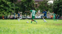 Pertandingan sepak bola dinamis yang dimainkan di lapangan berumput dengan para pemain yang antusias beraksi.