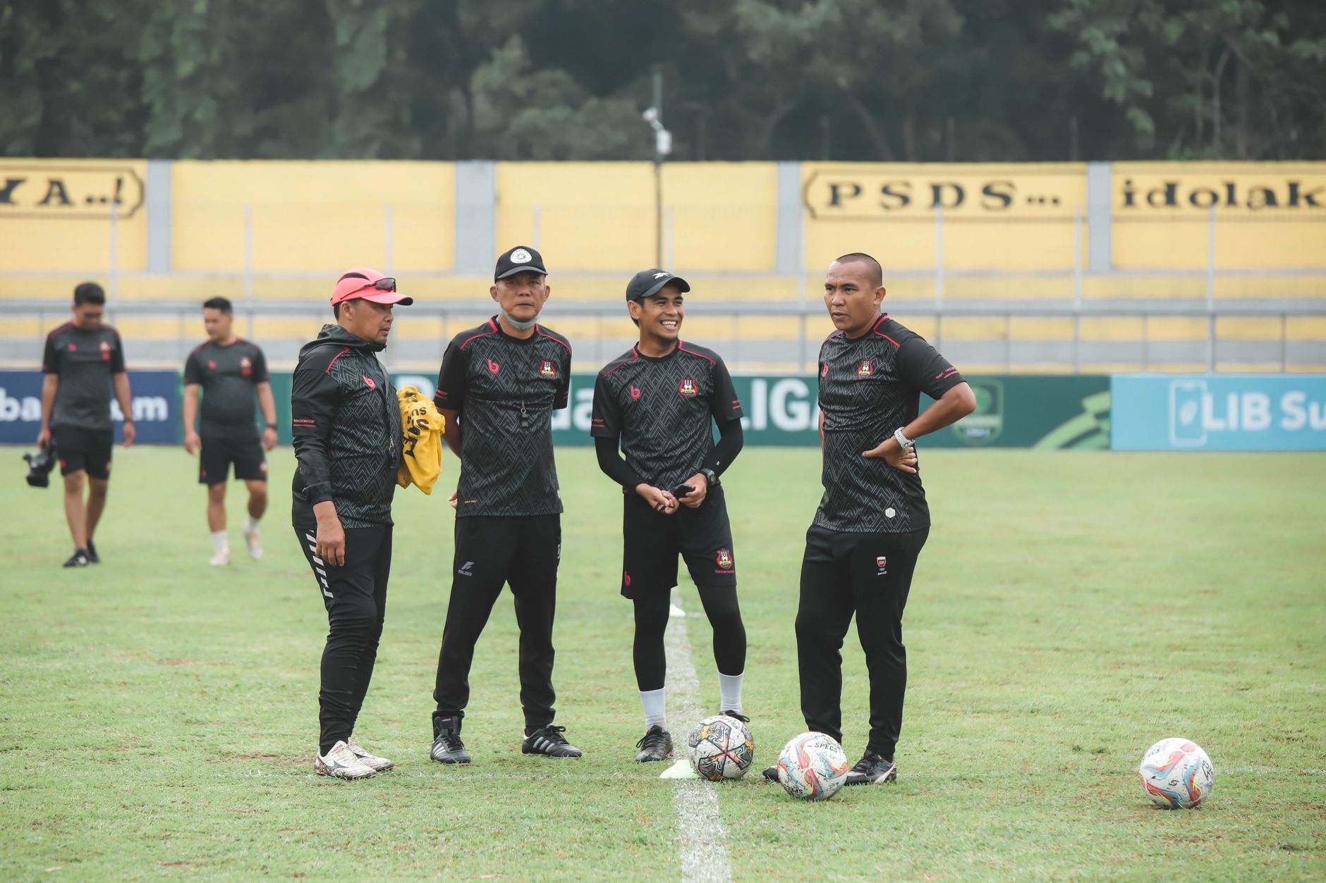 Sekelompok pelatih Indonesia berdiskusi di lapangan sepak bola di siang hari.