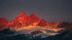 Pemandangan indah Pegunungan Alpen Swiss yang berbatu bersinar saat matahari terbenam dengan puncak bersalju.