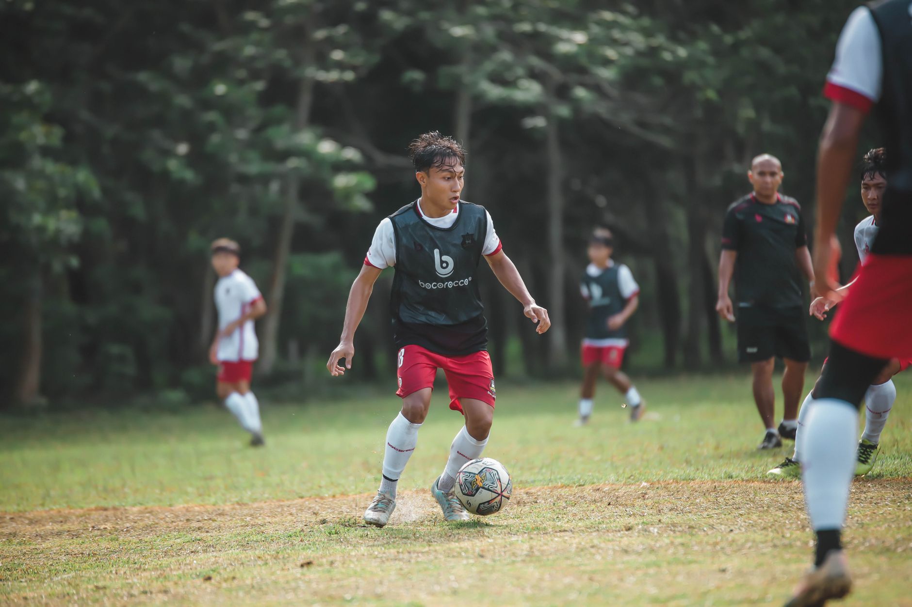 Pertandingan sepak bola remaja yang penuh aksi di hari yang cerah dengan pemain yang bergerak.