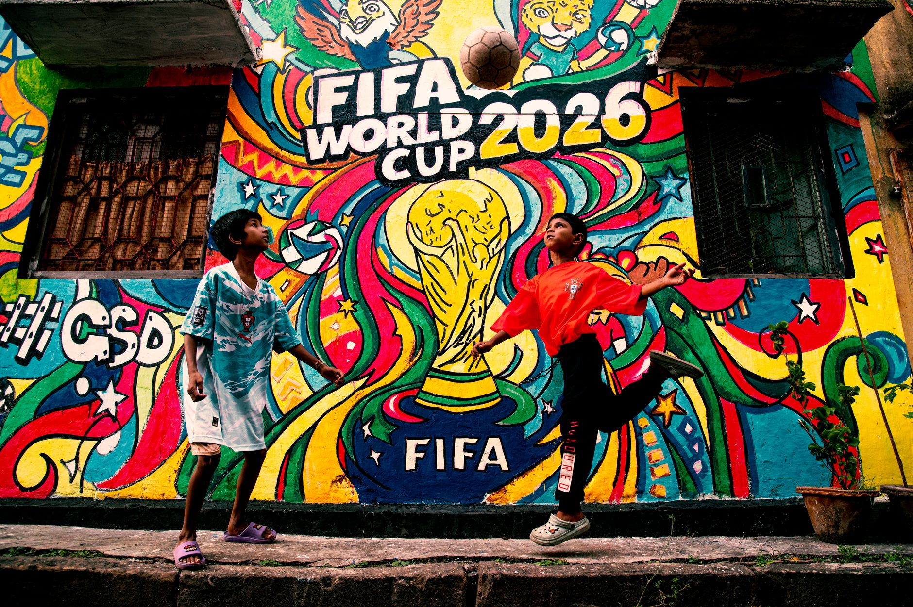 Mural berwarna-warni Piala Dunia FIFA 2026 dengan anak-anak bermain sepak bola di latar depan.