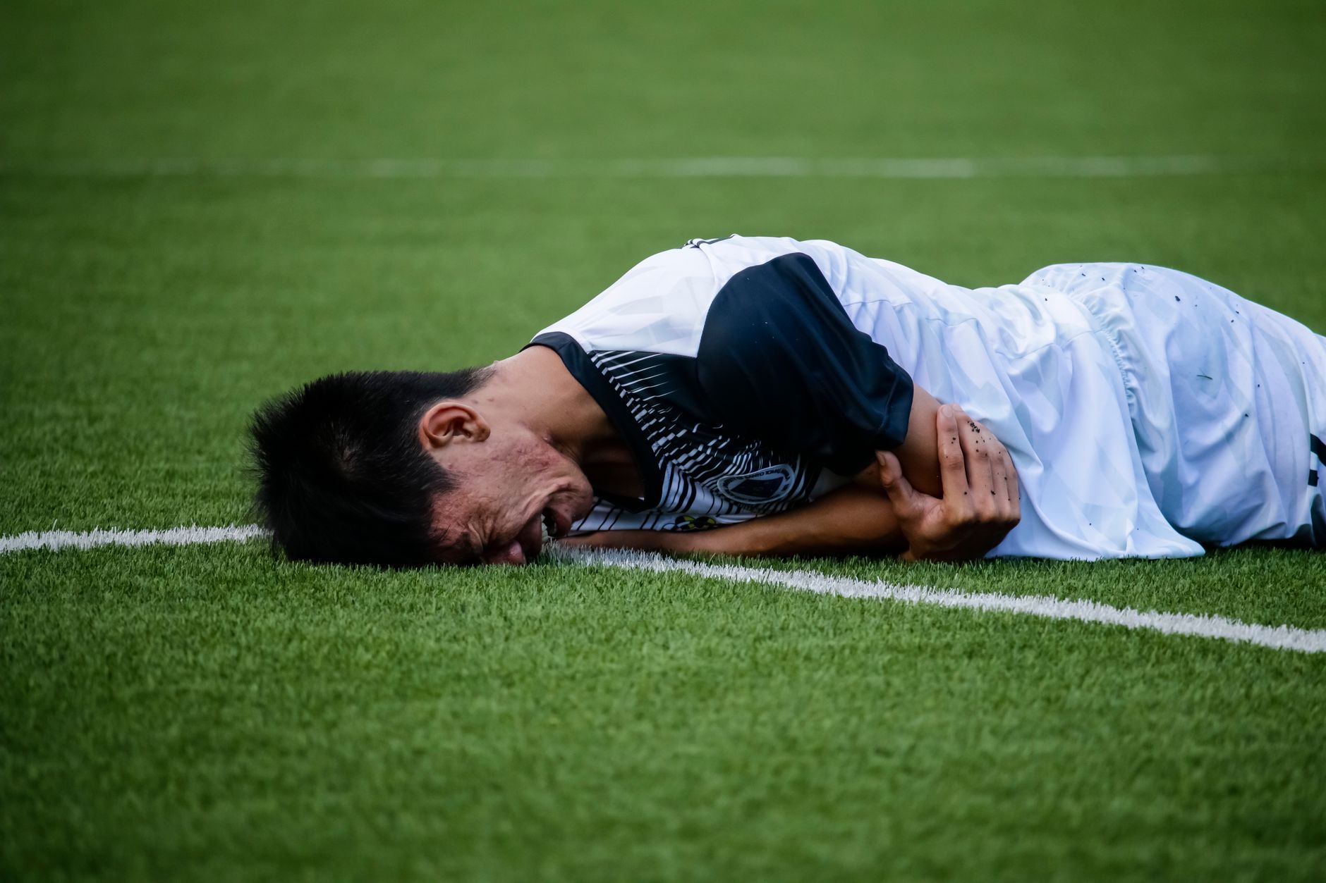 Pemain sepak bola tergeletak di lapangan kesakitan selama pertandingan, menunjukkan kemungkinan cedera.