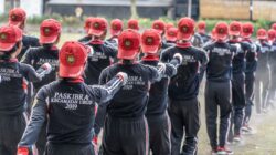 Sekelompok orang dalam seragam yang serasi dan topi merah berdiri dalam formasi di luar ruangan.