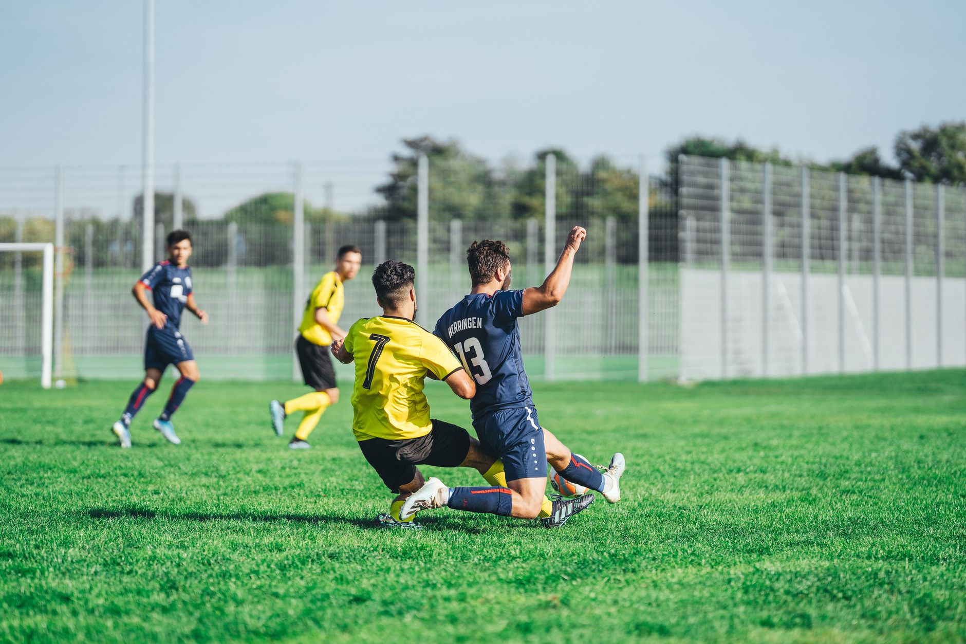 Pemain sepak bola dalam aksi selama pertandingan kompetitif di hari yang cerah di luar ruangan.
