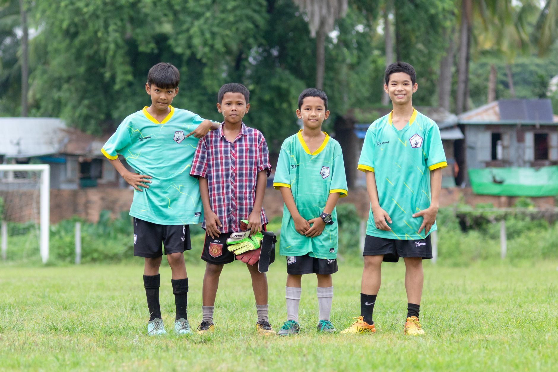 Empat anak laki-laki muda berseragam sepak bola berpose di lapangan rumput di Myawaddy, Myanmar.