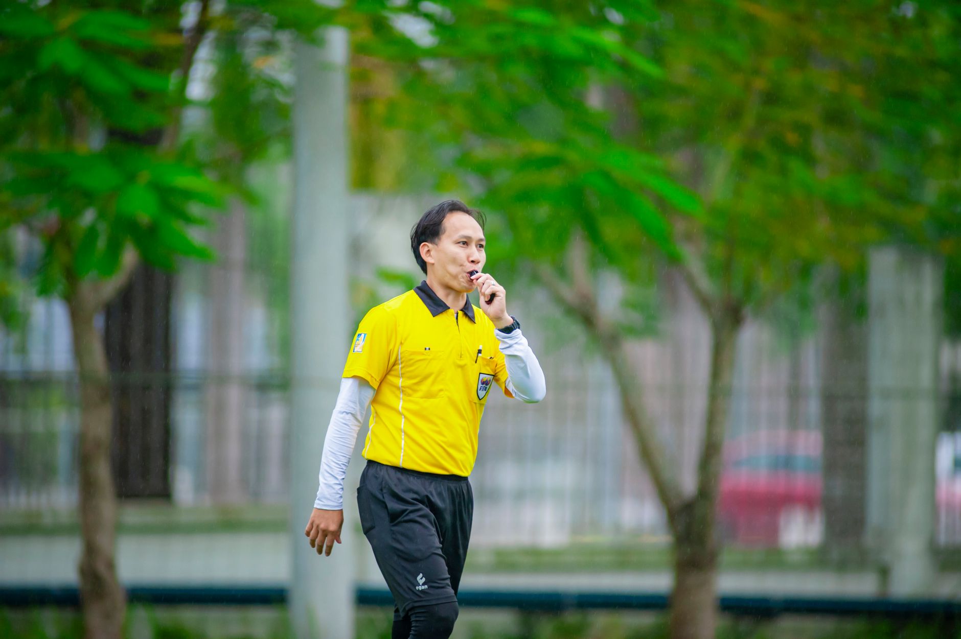 Seorang wasit berbaju kuning meniup peluit selama pertandingan sepak bola di Hanoi, Vietnam.