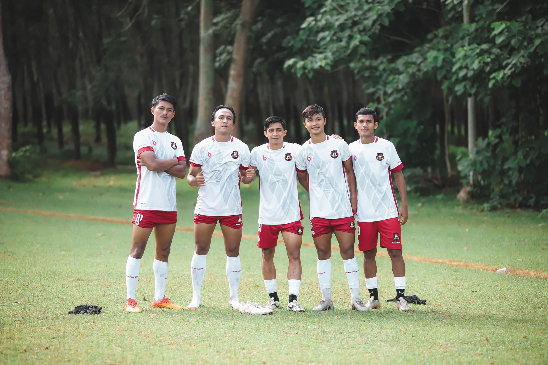 Sekel pemain sepak bola muda berpose dalam seragam tim di lapangan hijau yang subur. Pengaturan olahraga luar ruangan.