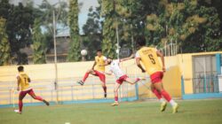 Pertandingan sepak bola penuh aksi di stadion Jakarta dengan pemain dalam gerakan yang ditangkap di suasana yang hidup.
