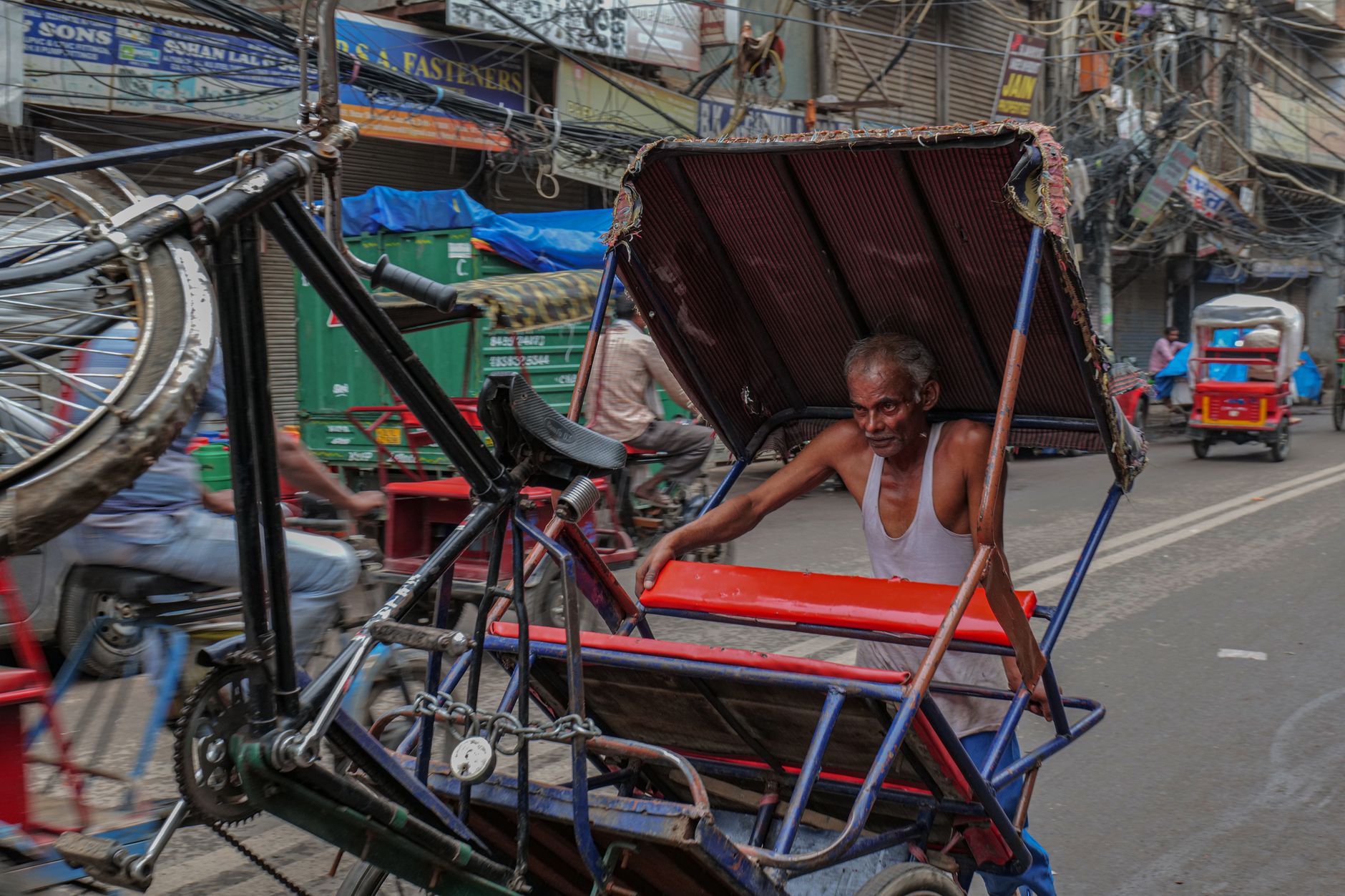 Seorang pria tua mengangkat rickshaw di jalan yang sibuk di Delhi, India, menunjukkan kehidupan jalanan yang cerah.