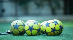 Empat bola sepak yang cerah beristirahat di lapangan rumput hijau.