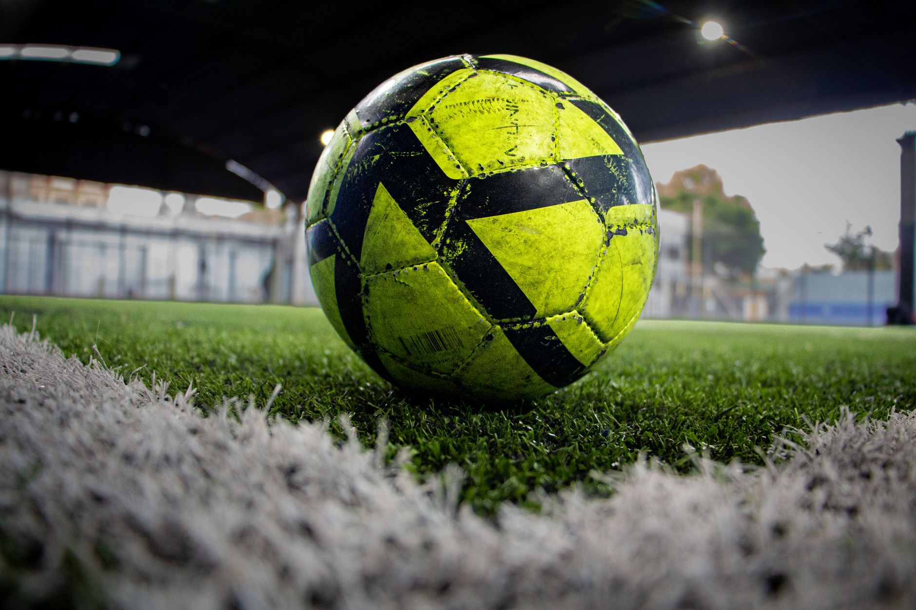 Gambar close-up bola sepak neon di lapangan rumput buatan di dalam ruangan.