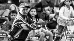 Foto monokrom yang menangkap orang-orang duduk di luar ruangan di Surabaya, Indonesia.