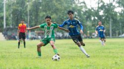 Para pemain terlibat dalam pertandingan sepak bola kompetitif di hari yang hujan.