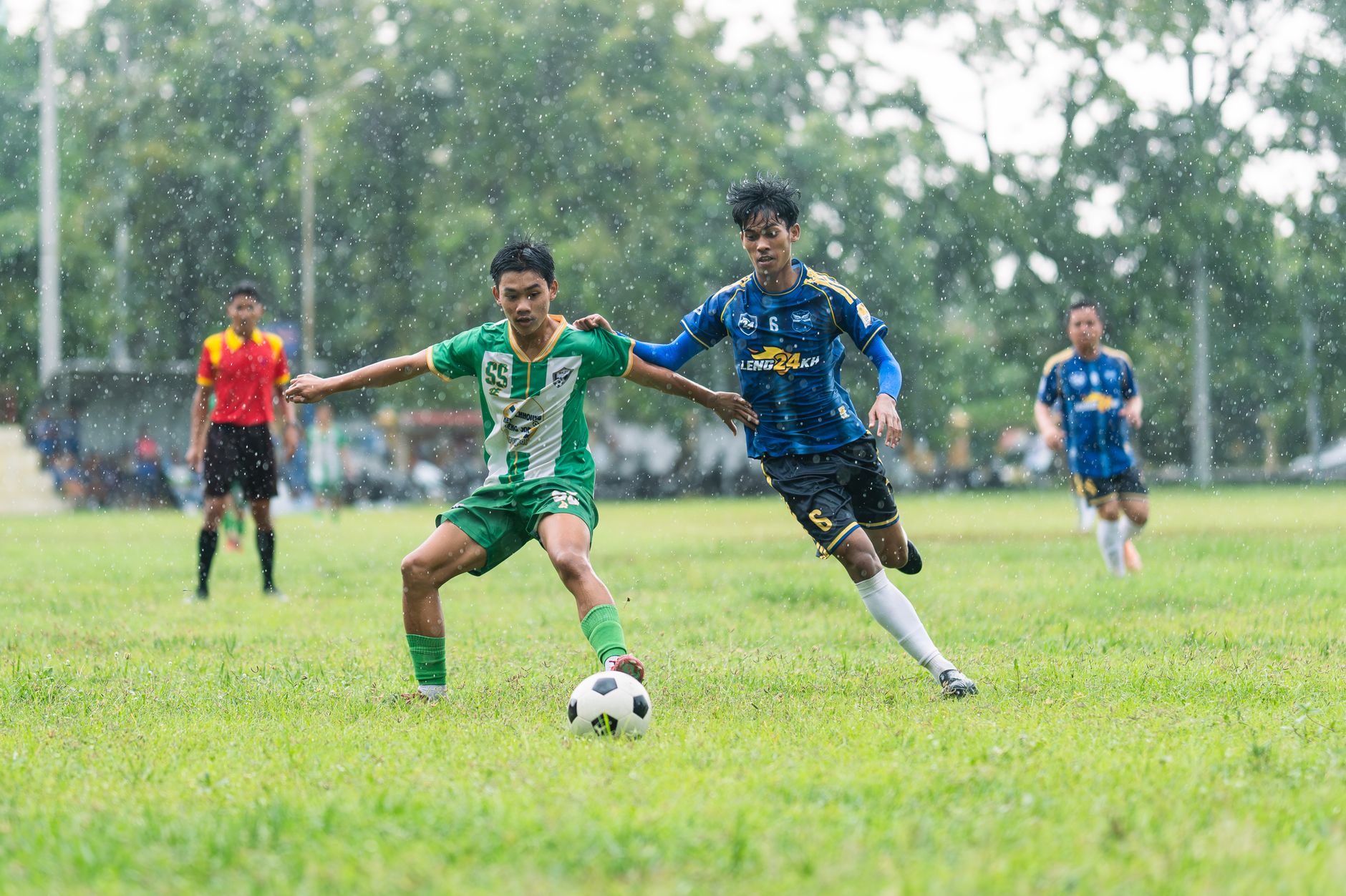 Para pemain terlibat dalam pertandingan sepak bola kompetitif di hari yang hujan.