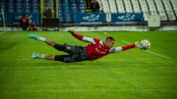 Seorang kiper sepak bola menyelam untuk membuat penyelamatan yang mengesankan selama pertandingan. Ditangkap di bawah lampu stadion.
