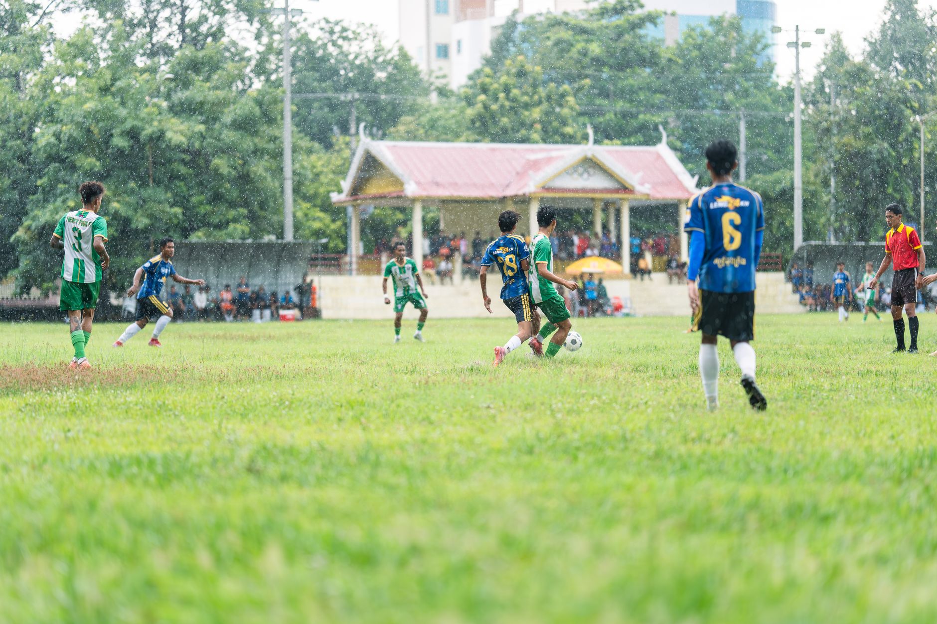 Para pemain sepak bola amatir berkompetisi di lapangan setempat pada hari hujan.