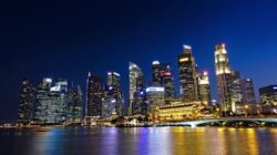 Pemandangan malam yang cerah dari cakrawala kota Singapura dengan gedung pencakar langit yang diterangi yang terpantul di air.