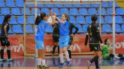 Momen penuh kebahagiaan saat gadis-gadis merayakan gol selama pertandingan sepak bola dalam ruangan. Semangat tim dan kegembiraan memenuhi gymnasium.