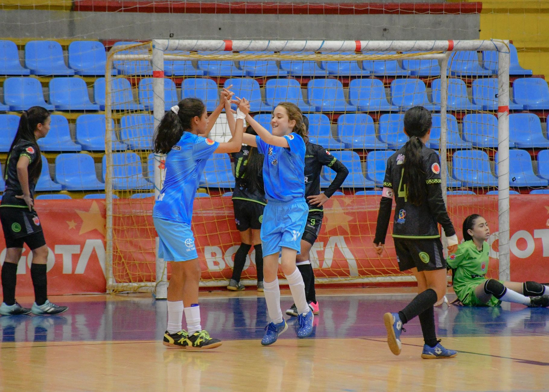 Momen penuh kebahagiaan saat gadis-gadis merayakan gol selama pertandingan sepak bola dalam ruangan. Semangat tim dan kegembiraan memenuhi gymnasium.
