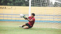 Seorang kiper beraksi menyelamatkan bola selama pertandingan sepak bola di lapangan.