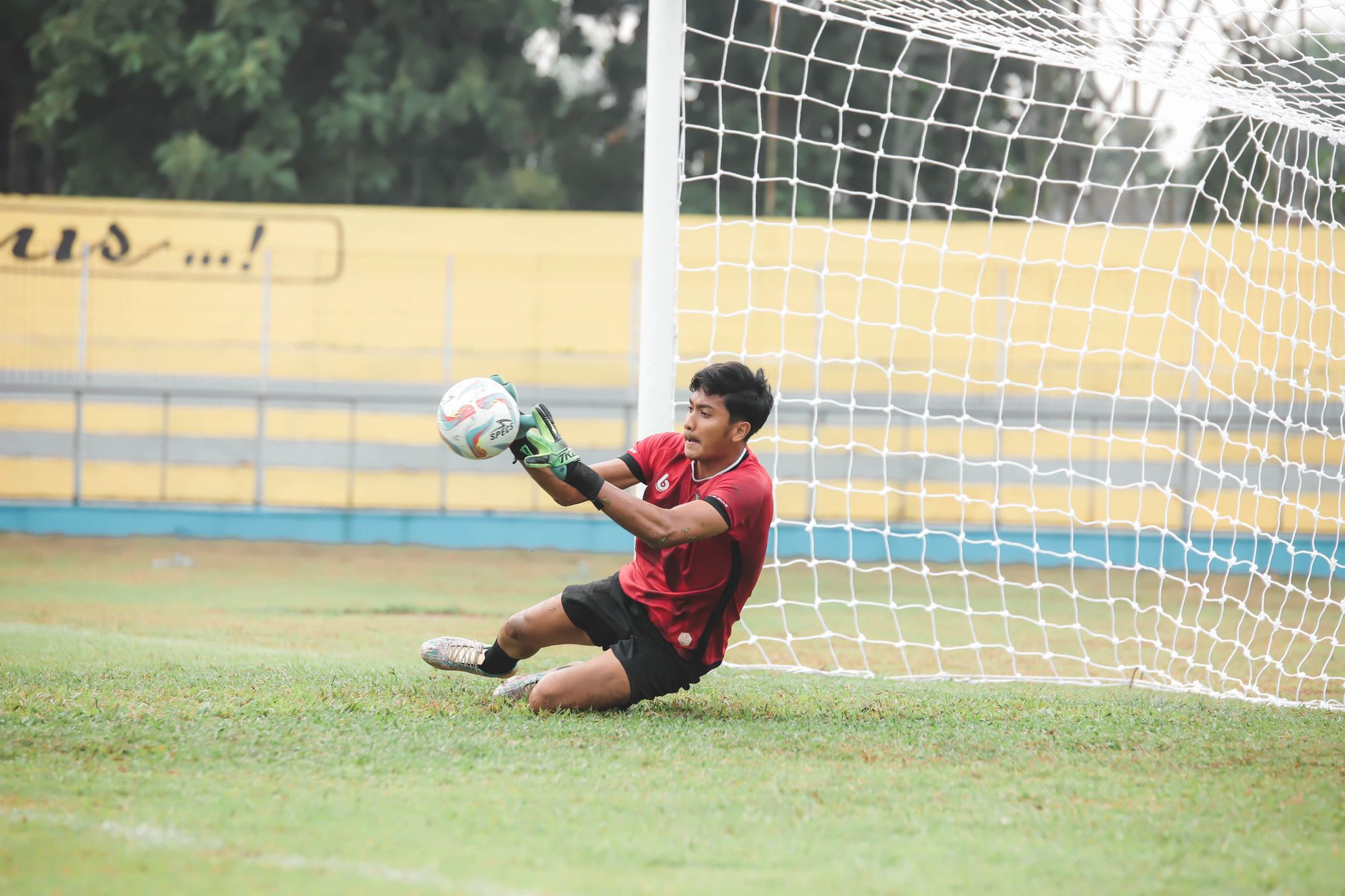 Seorang kiper beraksi menyelamatkan bola selama pertandingan sepak bola di lapangan.