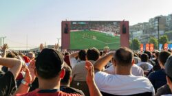 Kerumunan menonton pertandingan sepak bola di layar besar di luar ruangan di Istanbul, Türkiye.