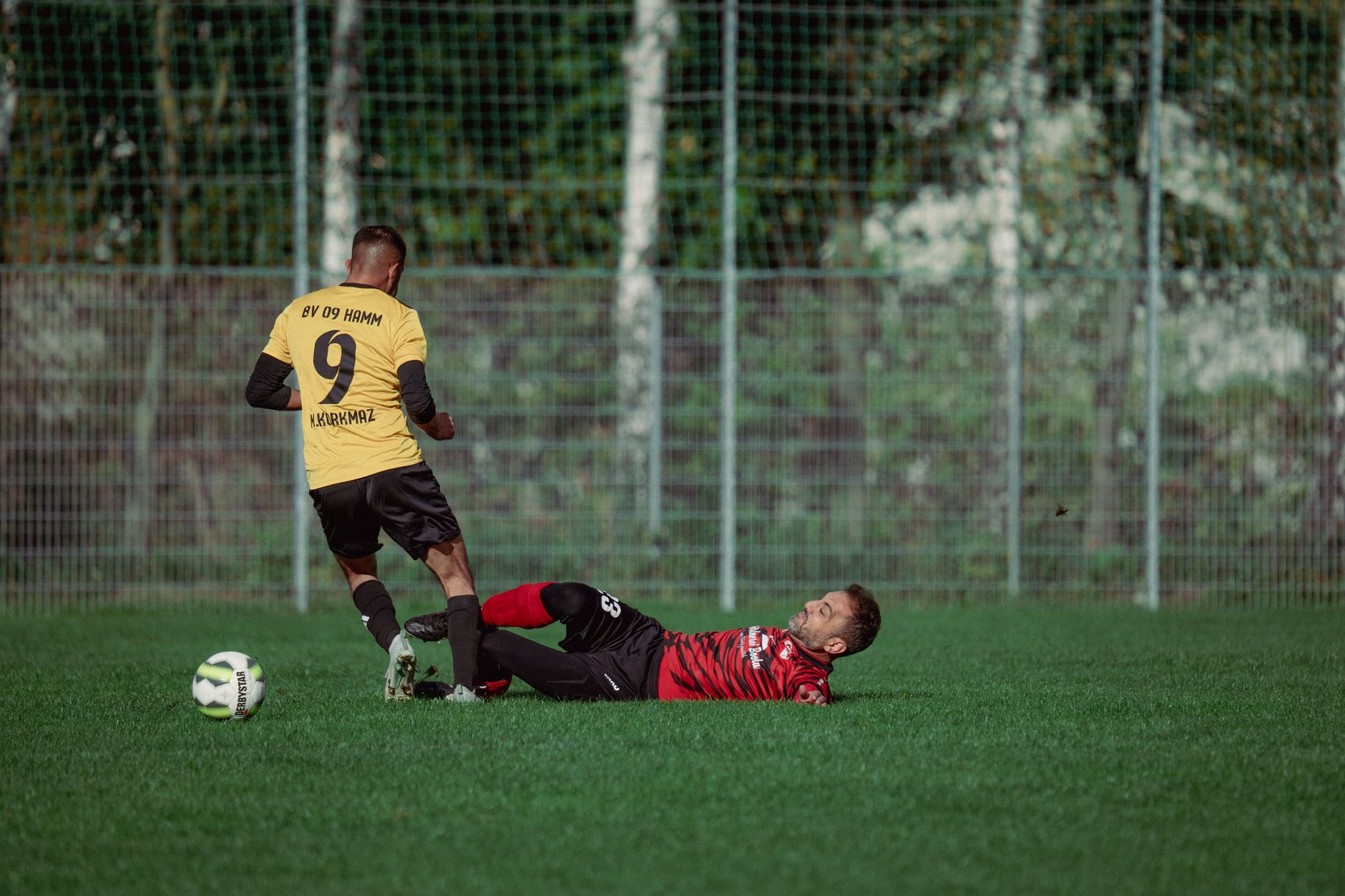 Dua pemain sepak bola dalam aksi dengan tekel dramatis di lapangan rumput selama pertandingan.