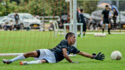 Kiper melompat menuju bola di lapangan sepak bola saat pertandingan.