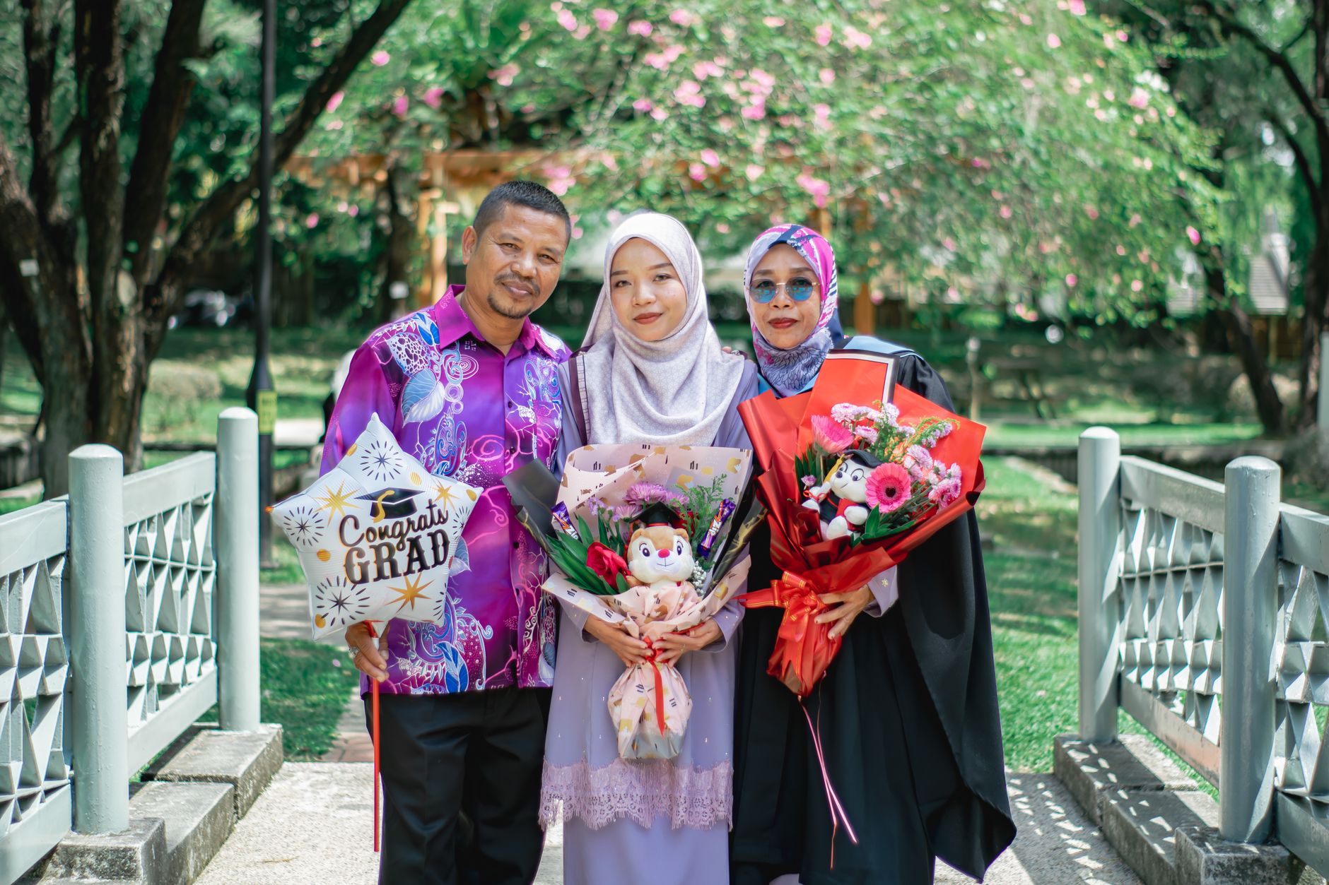 Sebuah keluarga merayakan kelulusan di luar ruangan di Shah Alam, Malaysia, menampilkan busana budaya dan kebahagiaan.
