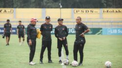 Sekelompok pelatih Indonesia berdiskusi di lapangan sepak bola di siang hari.