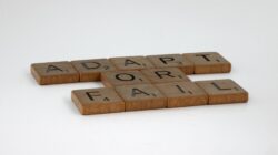 Ubin Scrabble mengeja 'Beradaptasi atau Gagal' di latar belakang polos, melambangkan pengambilan keputusan.