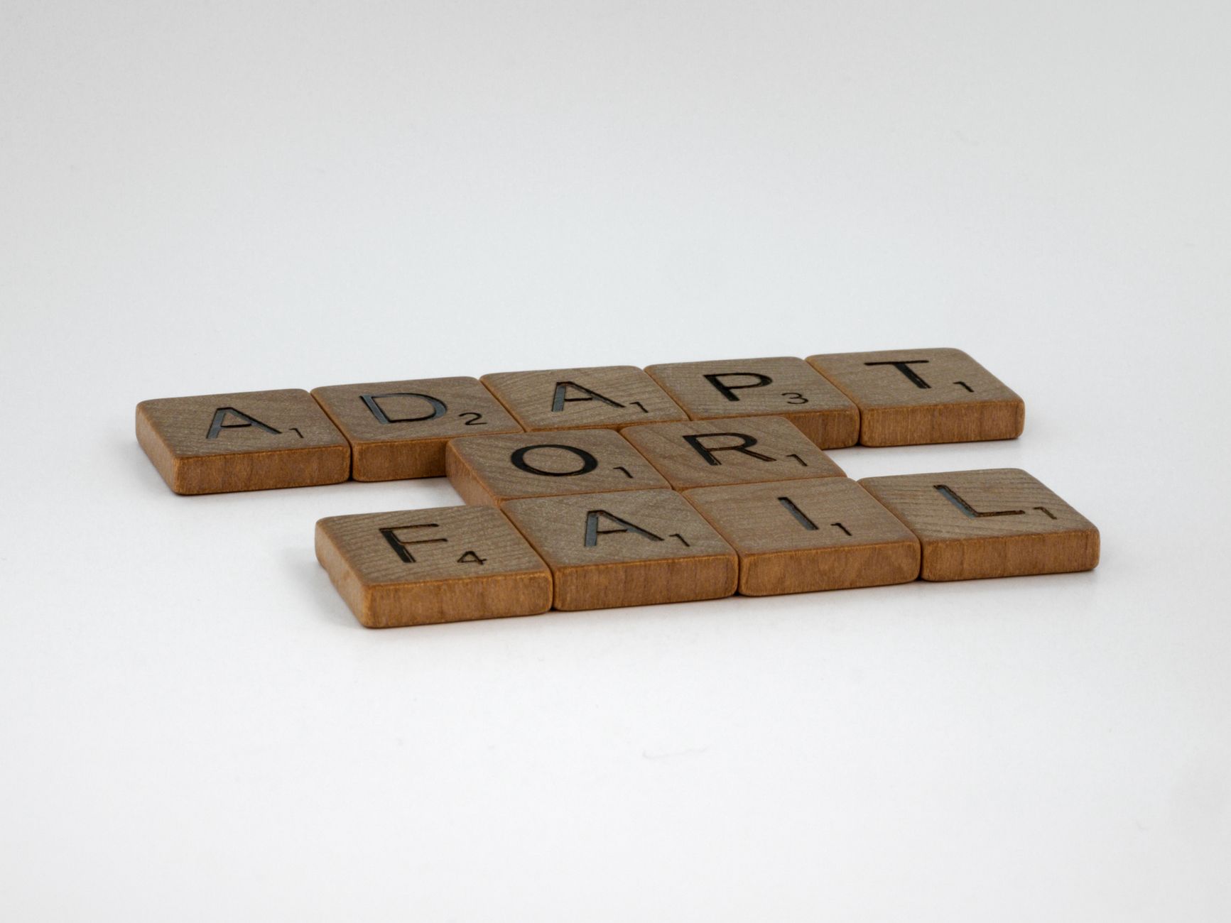 Ubin Scrabble mengeja 'Beradaptasi atau Gagal' di latar belakang polos, melambangkan pengambilan keputusan.