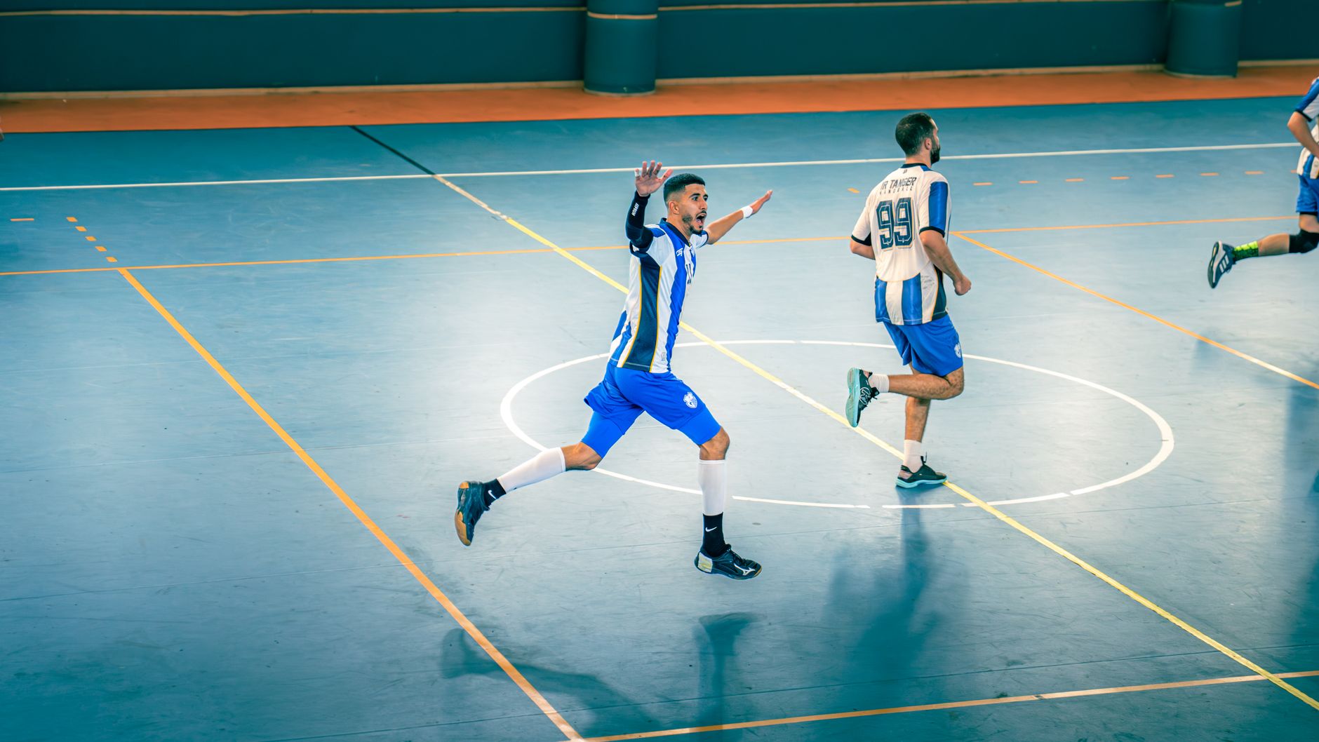 Pertandingan futsal dalam ruangan yang penuh aksi dengan pemain bergerak di lapangan.