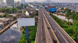 Pemandangan udara dinamis dari jalan tol di pemandangan kota Jakarta dengan garis langit dan sungai terlihat.