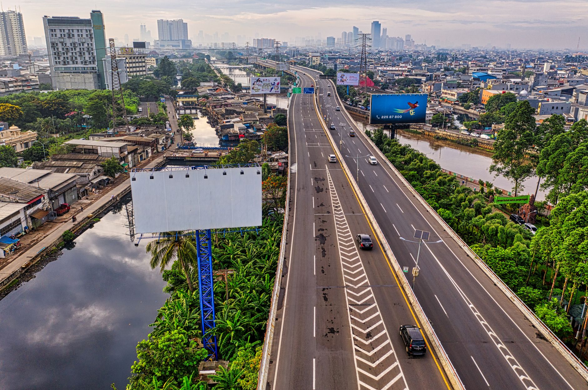 Pemandangan udara dinamis dari jalan tol di pemandangan kota Jakarta dengan garis langit dan sungai terlihat.