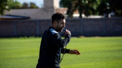 Pelatih sepak bola meniup peluit saat latihan di luar ruangan pada hari yang cerah.
